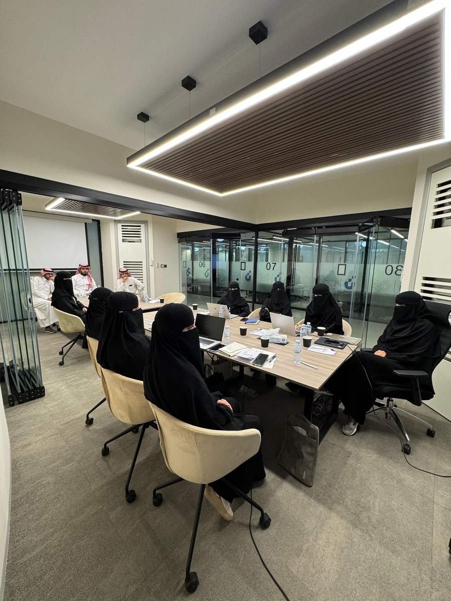 مساحة عمل مشتركة تضم عدة فرق حول طاولات اجتماعات وغرف زجاجية مرقّمة.